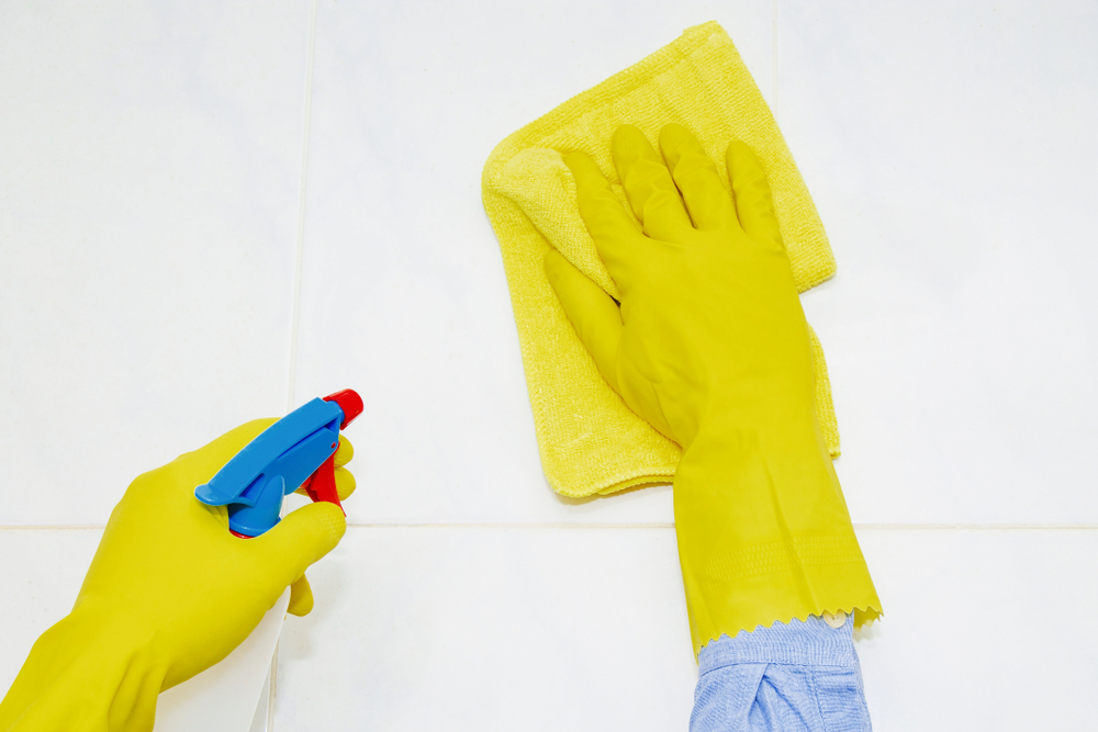 pessoa com luva nas duas mãos limpando azulejo com pano e produto