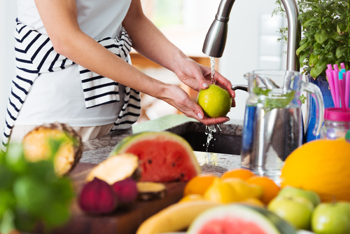 mulher lavando frutas na pia de uma cozinha