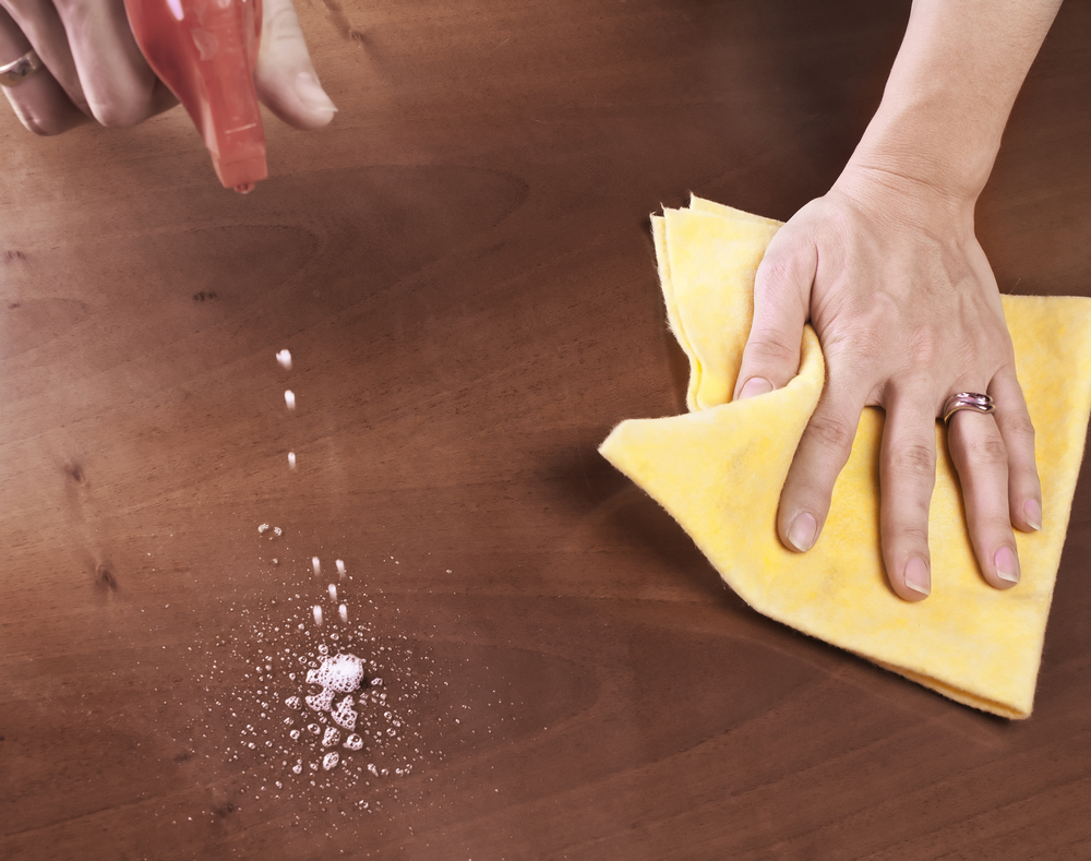 pessoa limpando uma superfície de madeira com um pano amarelo e um produto